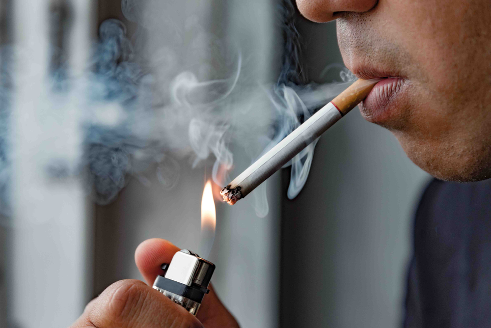 Man smoking a cigarette, exhaling smoke, highlighting the impact of smoking on dental health and implant success.